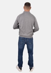 Felpa grigia con colletto alto, abbinata a jeans in denim blu. L'outfit è completato da sneakers bianche con accenti scuri.