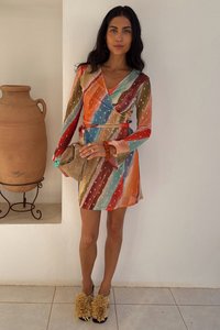 Daugiaspalvė apvyniojamojo stiliaus suknelė su ilgomis rankovėmis, puošta dryžuotais raštais raudonos, žalios ir smėlio spalvų, derinama su purių kulniukų batais ir maža rankine.