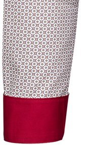 Tessuto di camicia bianca con un motivo geometrico in rosso e blu, rifinito con un polsino rosso solido alla fine delle maniche.