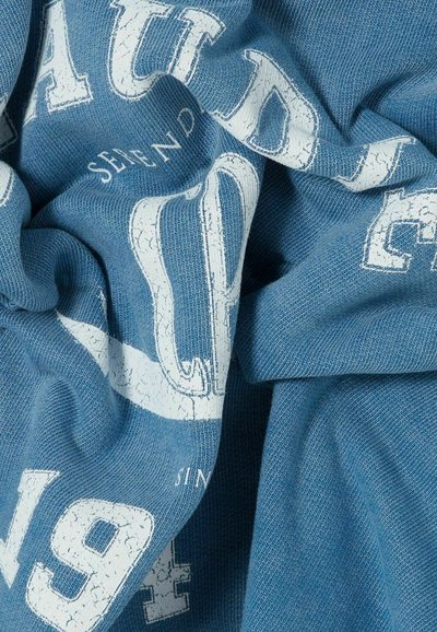 Il tessuto lavorato a maglia blu presenta una superficie testurizzata, con lettere e numeri bianchi in cattive condizioni in evidenza.