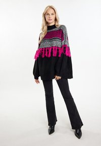 Maglione oversize nero con un motivo a maglia multicolore, caratterizzato da frange rosa all'orlo. Abbinate a pantaloni neri a zampa e stivali con punta.