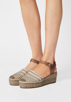 Sandales compensées avec une tige en tissu à motifs beige et rayures marron, bride de cheville réglable marron, et semelle en jute tissé.