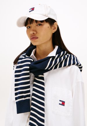 Casquette blanche avec logo brodé, écharpe rayée bleu et blanc, chemise blanche avec logo de poche, design minimaliste, textures lisses.