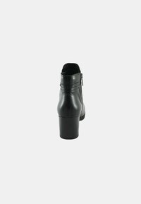 Stivaletto in pelle nera con tacco, dotato di chiusura a cerniera, superficie liscia e dettagli cuciti sul retro.