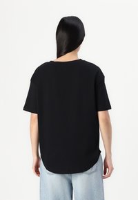 Svart kortermet t-skjorte med rund hals, løs passform og buet kant, sammen med lyseblå denimjeans. Ryddig, minimalistisk design.