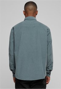 Knoopsluitingshirt in gedempt teal, met lange mouwen, een klassieke kraag, een afgeronde zoom en subtiele textuur. De achterkant toont knoopmanchetten.