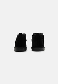 Botas de tobillo de ante negro con una textura suave, que presentan una suela de goma baja y una pequeña lengüeta en la parte posterior para ponerlas y quitarlas fácilmente.