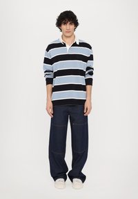 Rutet langermet polo i lys blå og marineblå med hvit krage, kombinert med løstsittende mørkeblå denimjeans med lappelommer.