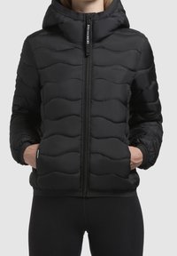 Czarna pikowana kurtka z zapięciem na zamek z przodu i kapturem. Posiada falisty wzór pikowania i elastyczne mankiety. Logo umieszczone po lewej stronie na piersi.