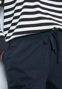 Marine joggers met een elastische tailleband en trekkoord. Gecombineerd met een gestreept shirt in marineblauw en crème, dat een casual stijl laat zien.