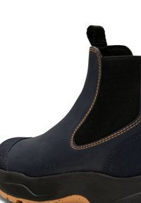 Bota Chelsea impermeable de color azul marino con lados elásticos, costuras en contraste de color marrón y suela de goma texturizada. Incluye una pestaña de tirón para facilitar su uso.