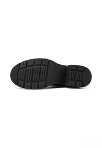 Suela de zapato de goma negra con un agarre texturizado y con patrón. Presenta tacos pronunciados y un diseño de punta redondeada. Perfil plano para estabilidad.