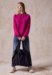 Felpa fucsia con motivo geometrico, con coulisse, abbinata a jeans blu e una grande borsa a tracolla nera. Le sneaker completano l'outfit.
