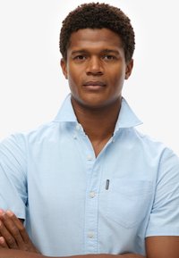 Błękitna koszula z krótkim rękawem, z klapą, kieszonką na lewej piersi oraz małą metką marki nad kieszonką.