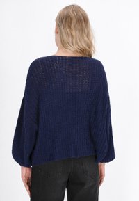 Dunkelblauer Strickpullover mit lockeren, weiten Ärmeln und einem strukturierten Muster. Der Saum ist leicht verkürzt und die Passform ist hinten entspannt.