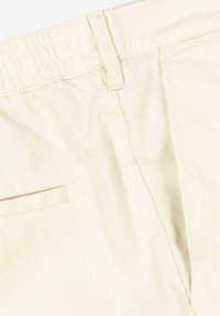 Beige cotton pants with an elastic waistband, featuring a side pocket and subtle texture. Clean design with no visible patterns or hardware.