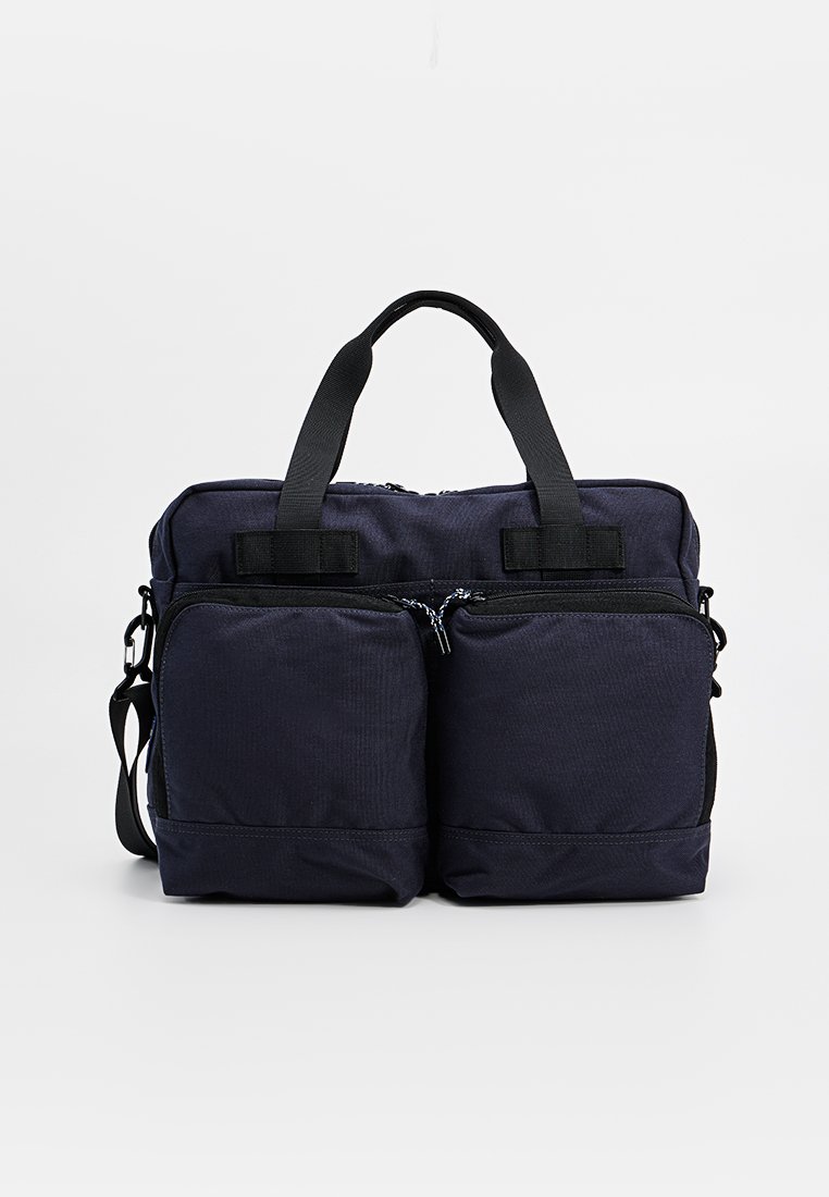 Bolso de tela azul marino con dos bolsillos frontales con cremallera, correa de hombro ajustable y dos asas superiores. Forma rectangular, material texturizado.