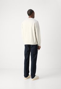 Creamfarbener Strickpullover mit gerippten Bündchen und Saum, kombiniert mit navyblauen Hosen. Die Schuhe sind weiß mit einer hellen Sohle und im flachen Design.