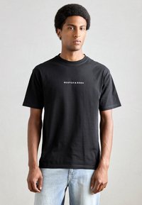 Black cotton t-shirt featuring a classic crew neck and short sleeves. 'Scotch & Soda' logo in white printed on the front.