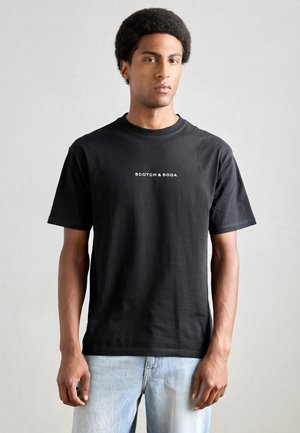 T-shirt en coton noir avec un col rond classique et des manches courtes. Logo 'Scotch & Soda' imprimé en blanc sur le devant.