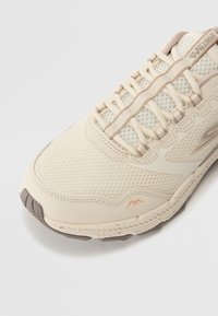 Chaussure de course en mesh beige avec des superpositions texturées, dotée d'un col rembourré, d'accents subtils et d'une semelle en caoutchouc flexible.