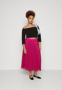 Čierny crop top bez ramienok, ružová plisovaná maxi sukňa a čierne ploché topánky. Strieborný náhrdelník a svetlomodrá crossbody taška.