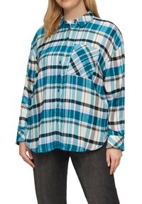 Camicia a quadri con bottoni, caratterizzata da motivi turchesi, neri e bianchi, con taschino sul petto, maniche lunghe e orlo arrotondato.