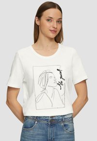 Witte katoenen t-shirt met een zwarte lijntekening van een gezicht en de tekst "Wees jezelf" in een rechthoekig ontwerp. Korte mouwen en een relaxte pasvorm.