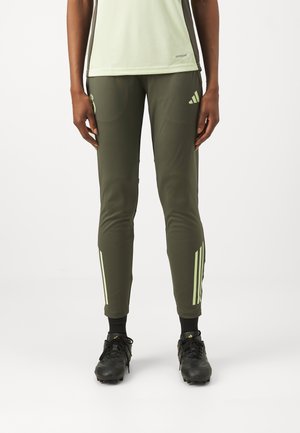 Olivengrønne treningsbukser med en kroppsnær design, med lysegrønne striper på sidene og smale ankler. Brukt med svarte fotballsko.