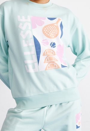 Jasnoniebieska bluza i spodnie z kolorową abstrakcyjną grafiką o tematyce tenisowej oraz napisem "ELLESSE" na piersi i nodze.
