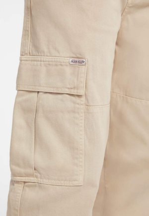 Calças cargo bege com bolsos de remendo, tecido durável e um pequeno rótulo de logo. Textura suave com detalhes de costura visíveis.