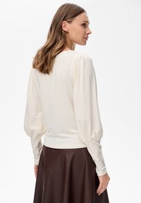 Cremfarbene Langarmbluse mit puffigen Ärmeln und bestickten Akzenten an den Handgelenken, kombiniert mit einem dunkelbraunen Lederrock.