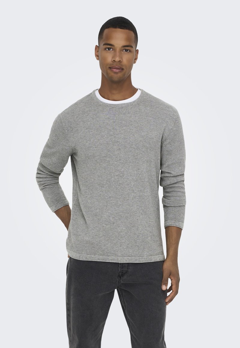 Grey textured long-sleeve shirt with a white crew neckline, featuring a relaxed fit and ribbed cuffs, paired with dark jeans.
