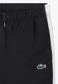 Μαύρα αθλητικά σορτς με υφασμάτινη υφή, ελαστική μέση και λευκές πλευρικές ρίγες. Διακοσμούνται με πράσινο, κεντητό λογότυπο κροκοδείλου.