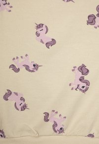 Tissu beige clair présentant un motif répété de licornes roses avec des crinières violettes, illustrées dans diverses poses, texture douce.