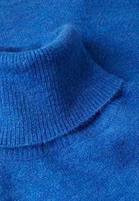 Gros plan sur un tissu doux de pull à col roulé bleu tricoté, montrant le col côtelé et le motif de tricot texturé.