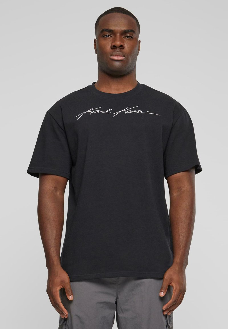 T-shirt en coton noir à manches courtes et col rond, avec du texte en cursive blanche sur la poitrine. Design simple et décontracté.