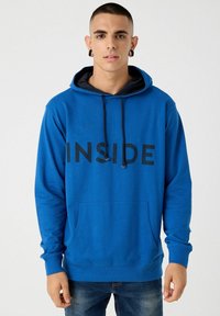 Sudadera azul con capucha y bolsillo frontal, con un gráfico negro que dice "INSIDE", terminada con capucha ajustable y puños acanalados.