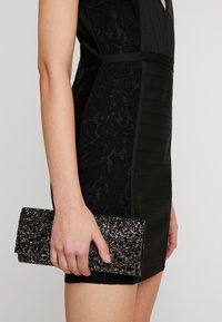 Pochette noire ornée avec une surface texturée, présentant une finition étincelante. La robe assortie possède des détails en dentelle et en tissu canalé.