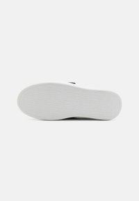 Egy cipő talpa, fehér gumiból készült, kiemelkedő "DKNY" feliratos mintázattal. Simma felület, lekerekített él, minimalista dizájn.