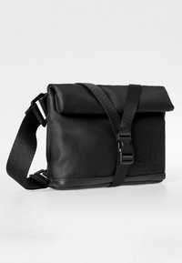 Black messenger bag with a fold-over top, made of smooth synthetic material. Features an adjustable strap and embossed brand logo on the side.