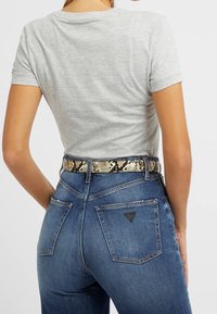 T-shirt grigio aderente con maniche corte abbinato a jeans in denim blu scuro a vita alta. Accenti distintivi di una cintura in stampa rettile in vita.