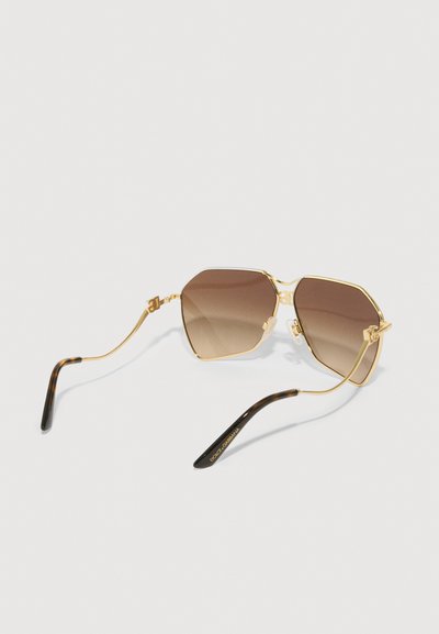 Sunglase s okvirom od zlata s smešnim gradijentnim lećama, oktagonalnog oblika, sa prozirnim nosačima i crnim tortoiseshell rukama.