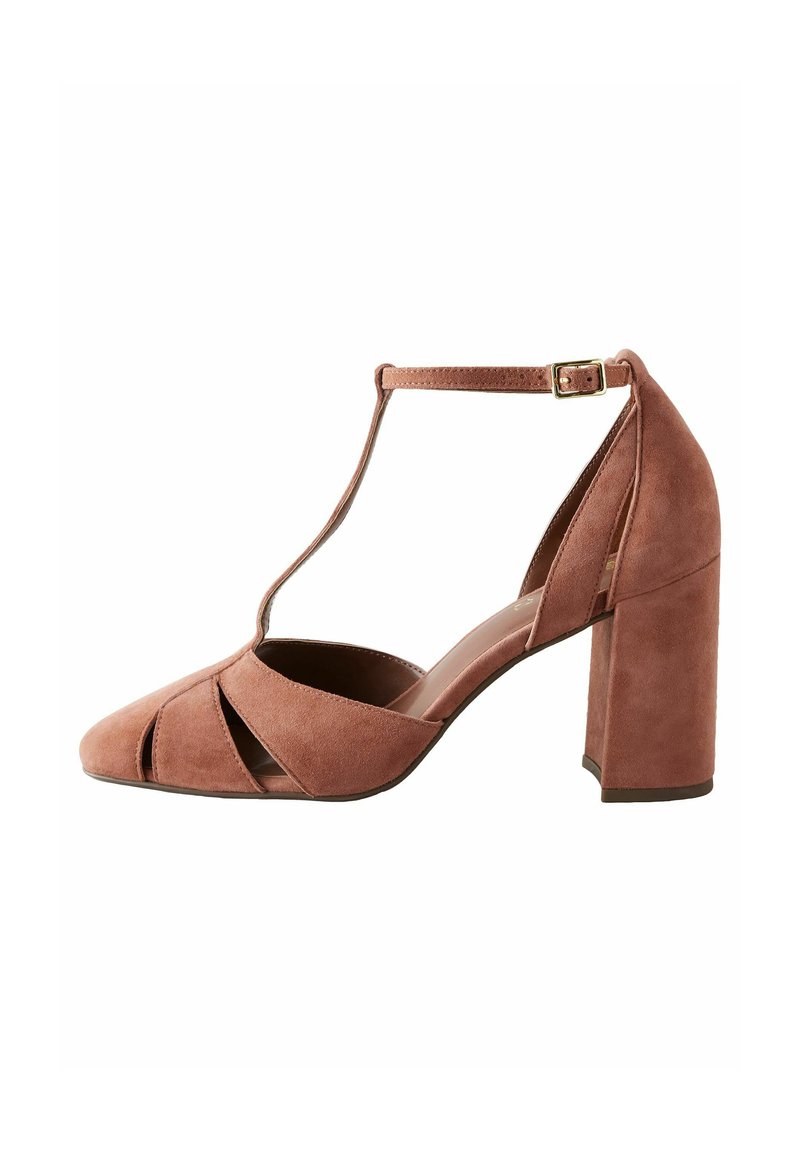 Pompe à talons hauts en daim rose avec un design à T, bout arrondi et découpes. Présente un talon épais et carré. Bride à la cheville ajustable.