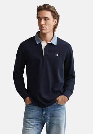 Polo à manches longues bleu marine avec un col en denim clair, doté d'une patte de boutonnage blanche et d'un logo brodé sur la poitrine. Matière en coton douce.