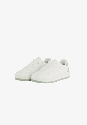 Baskets blanches de sport avec une finition texturée, présentant un accent vert au niveau du talon et une semelle plate en caoutchouc. Design classique avec lacets.