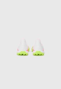 White athletic shoes featuring pink accents and a bright green textured sole, with a streamlined design and minimalistic construction.