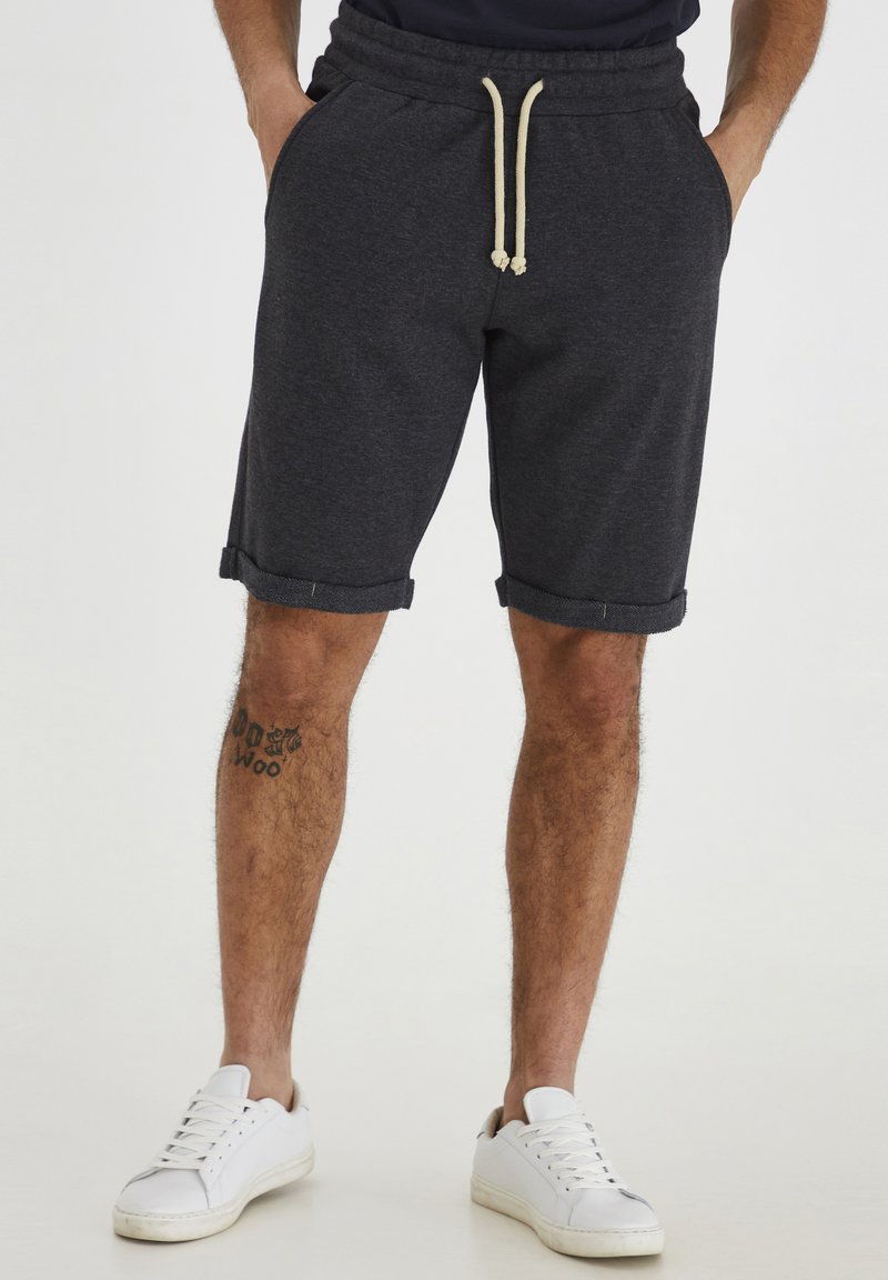Shorts en mélange de coton gris foncé avec taille élastique, cordon beige et ourlets retroussés ; associés à des baskets blanches.