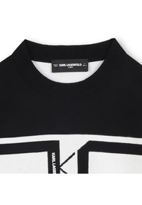 Juodas ir baltas megztinis su ribotu apvaliu kaklu. Pažymėtas ryškiu logotipo raštu ir audinio etikete su užrašu „KARL LAGERFELD KIDS“.
