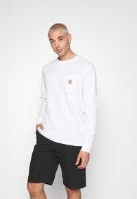 Langermet hvit skjorte med brystlomme som har logo. Kombinert med svarte cargo-shorts. Glatt stoff, avslappet passform og enkelt design.